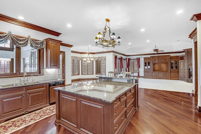 kitchen featuring light stone countertops, sink, hanging light fixtures, a kitchen island, and ceiling fan with notable chandelier