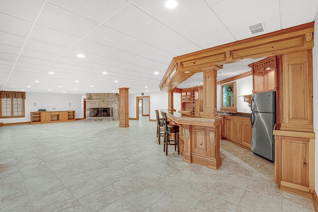 kitchen featuring a breakfast bar, a center island, a stone fireplace, ornate columns, and stainless steel refrigerator