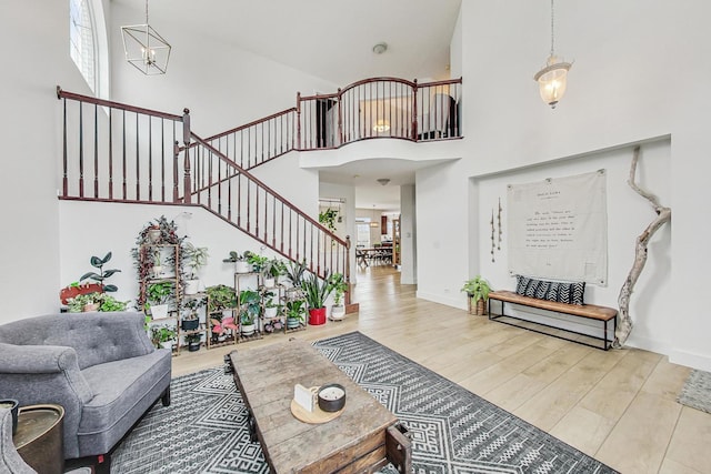 living room with a towering ceiling, a chandelier, and light wood-type flooring