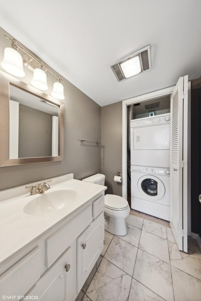 bathroom with vanity, stacked washer and clothes dryer, and toilet