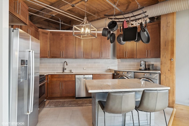 kitchen featuring pendant lighting, backsplash, sink, appliances with stainless steel finishes, and washing machine and clothes dryer