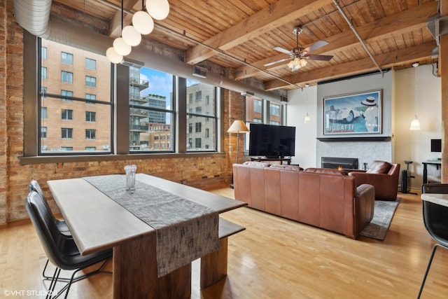 living room with ceiling fan, light hardwood / wood-style floors, beam ceiling, and brick wall