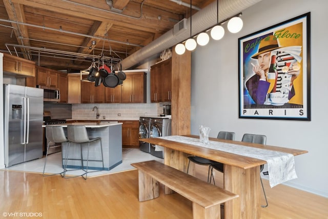 kitchen featuring stainless steel appliances, washing machine and clothes dryer, a center island, hanging light fixtures, and a breakfast bar area