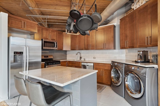 kitchen featuring decorative backsplash, a kitchen bar, stainless steel appliances, washer and clothes dryer, and sink