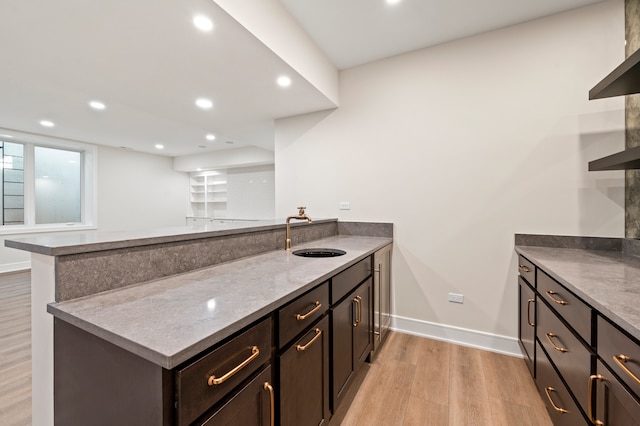 kitchen with dark brown cabinetry, stone counters, sink, light hardwood / wood-style flooring, and kitchen peninsula