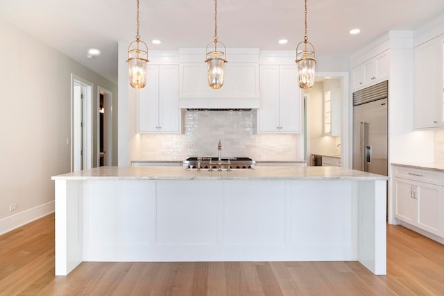 kitchen featuring light stone countertops, light wood-type flooring, white cabinets, a center island, and built in refrigerator