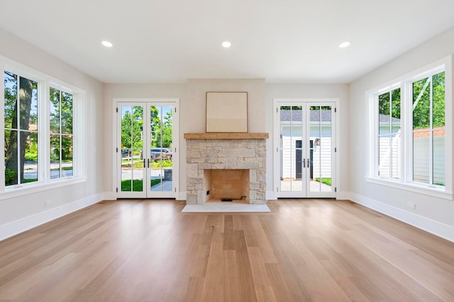 unfurnished living room with french doors, light hardwood / wood-style flooring, plenty of natural light, and a stone fireplace