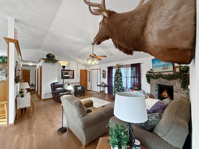 living room featuring a brick fireplace, ceiling fan, light wood-type flooring, and vaulted ceiling