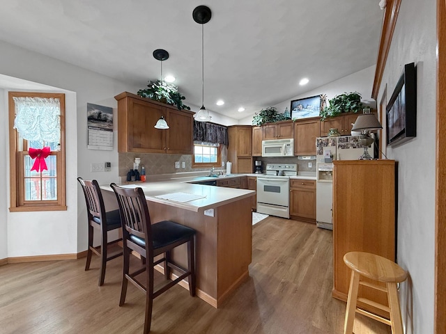 kitchen featuring a kitchen breakfast bar, kitchen peninsula, light hardwood / wood-style floors, decorative light fixtures, and white appliances