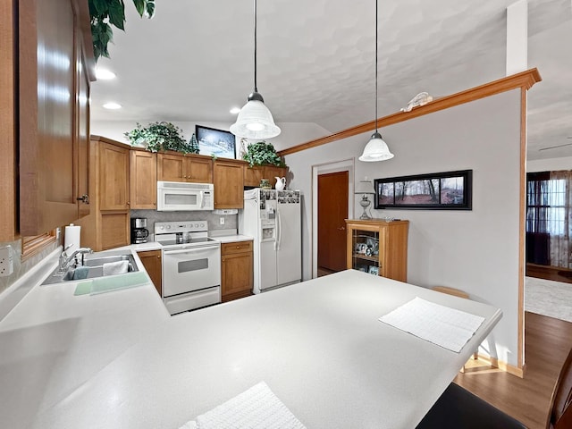 kitchen with hardwood / wood-style floors, white appliances, sink, decorative light fixtures, and kitchen peninsula