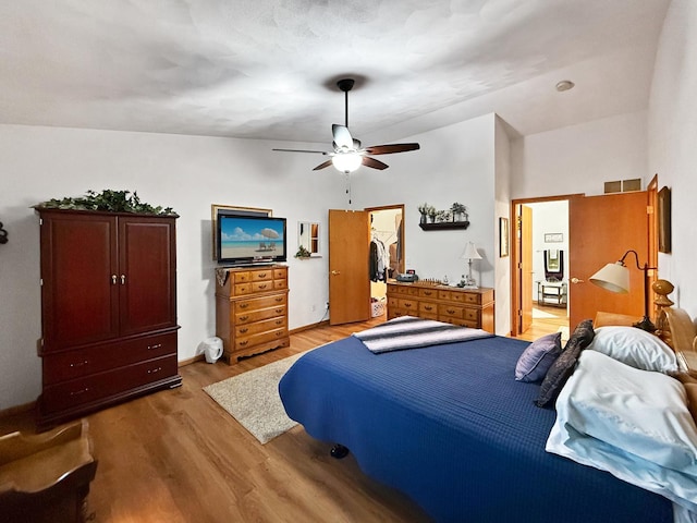 bedroom featuring a walk in closet, vaulted ceiling, ceiling fan, light hardwood / wood-style flooring, and a closet