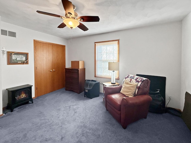 living area featuring a wood stove, ceiling fan, and carpet floors