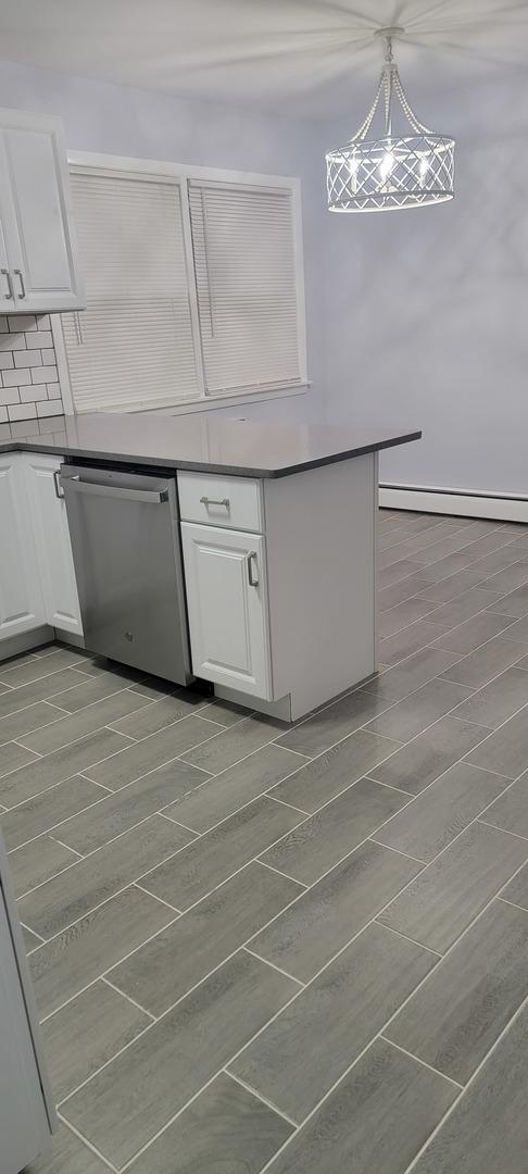 kitchen with backsplash, pendant lighting, a baseboard radiator, dishwasher, and white cabinetry