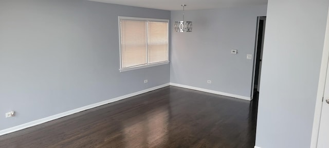 spare room with an inviting chandelier and dark wood-type flooring