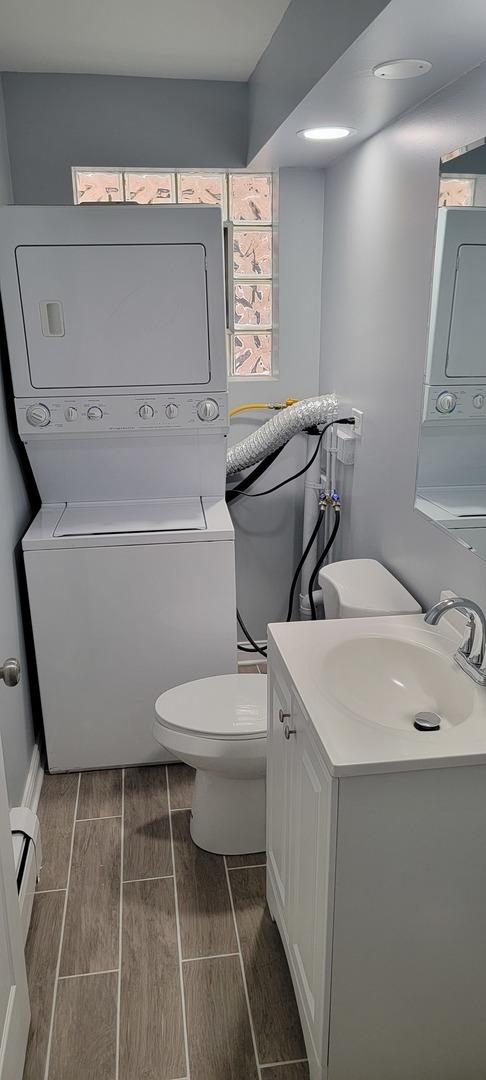 bathroom with stacked washer / drying machine, toilet, and vanity