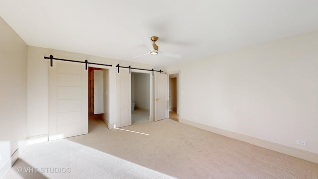 unfurnished bedroom with ceiling fan, a barn door, and carpet floors