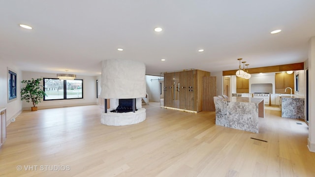 unfurnished living room with a multi sided fireplace, light wood-type flooring, and sink