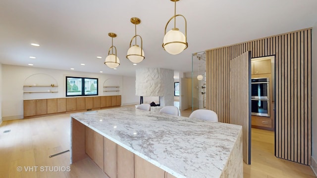 kitchen featuring double oven, light hardwood / wood-style floors, light stone counters, and hanging light fixtures