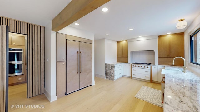 kitchen with white cabinets, sink, light wood-type flooring, light stone counters, and stainless steel appliances