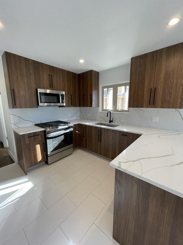 kitchen with sink, dark brown cabinets, stainless steel appliances, tasteful backsplash, and light stone countertops