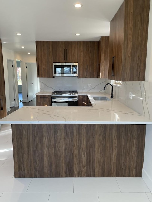 kitchen with tasteful backsplash, appliances with stainless steel finishes, sink, and kitchen peninsula