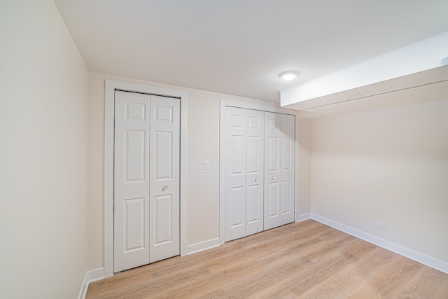 unfurnished bedroom featuring multiple closets and light hardwood / wood-style floors