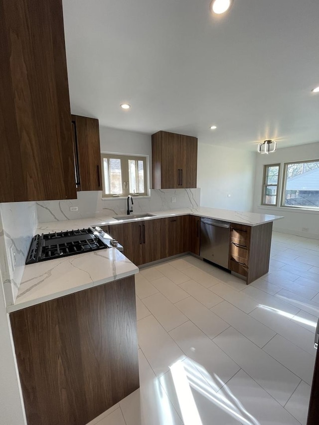 kitchen with sink, dishwasher, light stone countertops, a healthy amount of sunlight, and kitchen peninsula