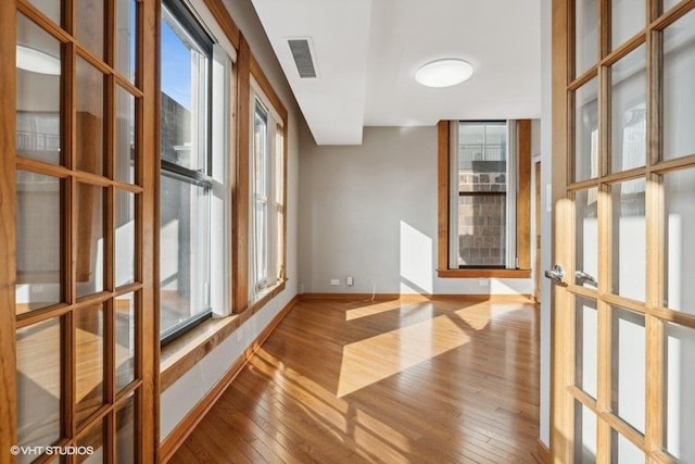 empty room with plenty of natural light, wood-type flooring, and french doors