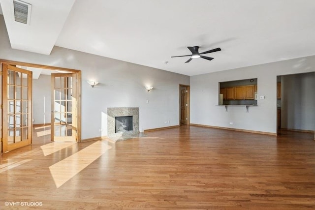 unfurnished living room featuring ceiling fan, a fireplace, french doors, and light hardwood / wood-style flooring