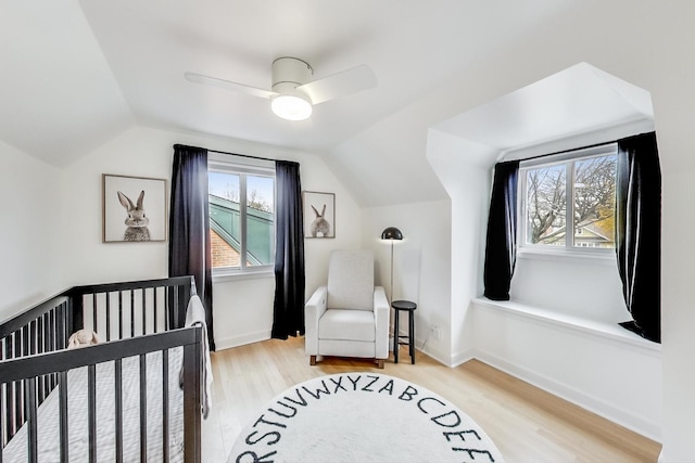 bedroom with light wood-type flooring, ceiling fan, lofted ceiling, and a nursery area