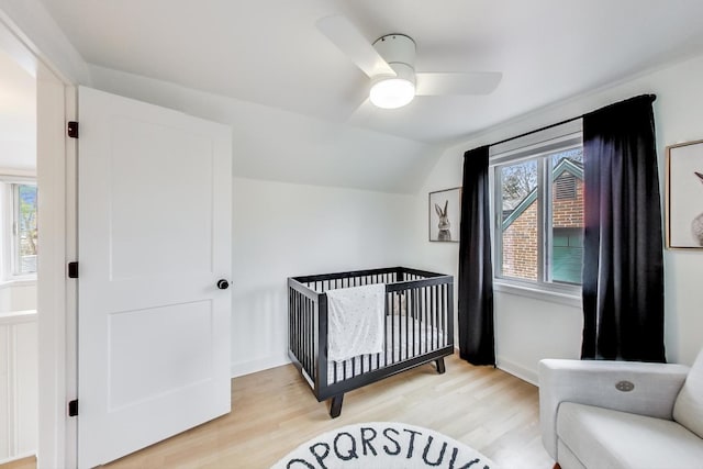 bedroom featuring ceiling fan, light hardwood / wood-style floors, a nursery area, and lofted ceiling