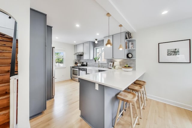 kitchen featuring pendant lighting, stainless steel appliances, kitchen peninsula, light wood-type flooring, and a breakfast bar area