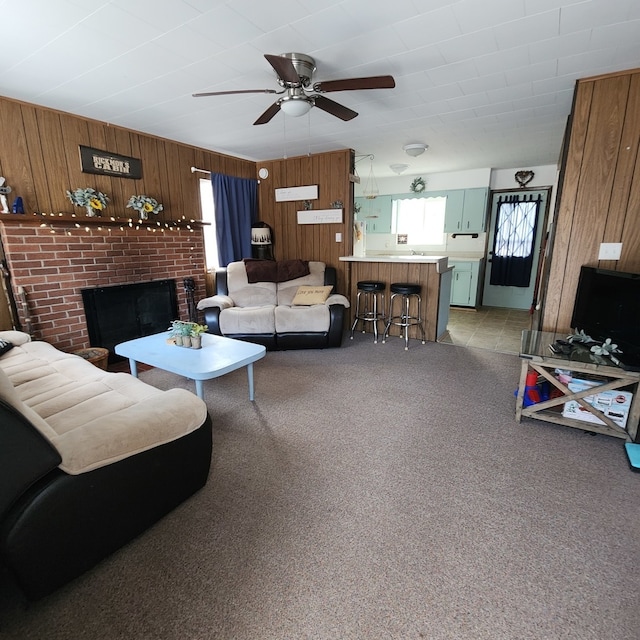 carpeted living room with wooden walls, ceiling fan, and a brick fireplace