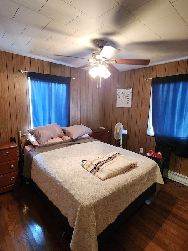 bedroom featuring dark hardwood / wood-style flooring, baseboard heating, ceiling fan, and wooden walls