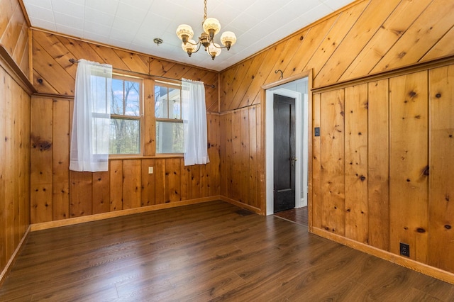 spare room featuring a notable chandelier, wood walls, and dark hardwood / wood-style flooring