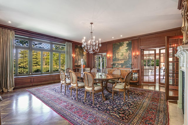 dining room featuring wood walls, parquet floors, french doors, an inviting chandelier, and ornamental molding