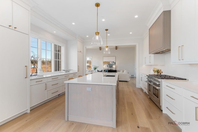 kitchen featuring sink, double oven range, pendant lighting, a kitchen island with sink, and white cabinets