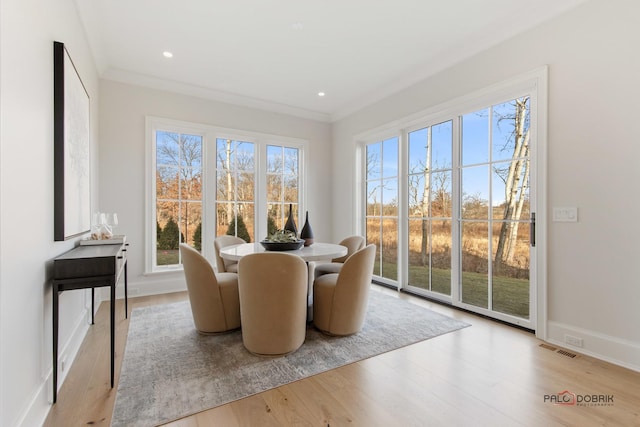 dining space featuring light hardwood / wood-style flooring, ornamental molding, and a healthy amount of sunlight