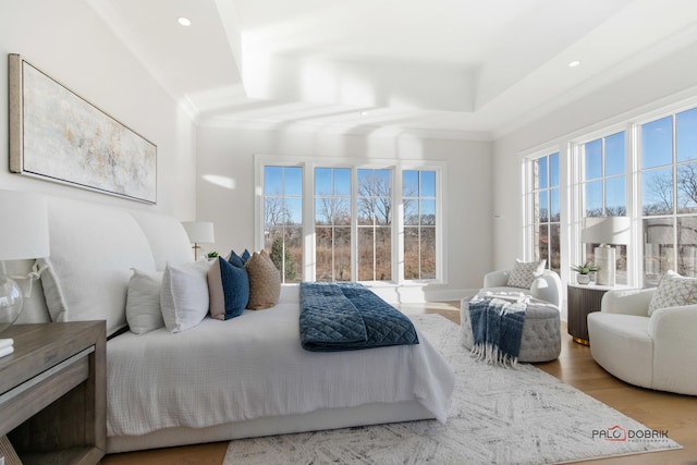 bedroom with ornamental molding, light wood-type flooring, and a tray ceiling