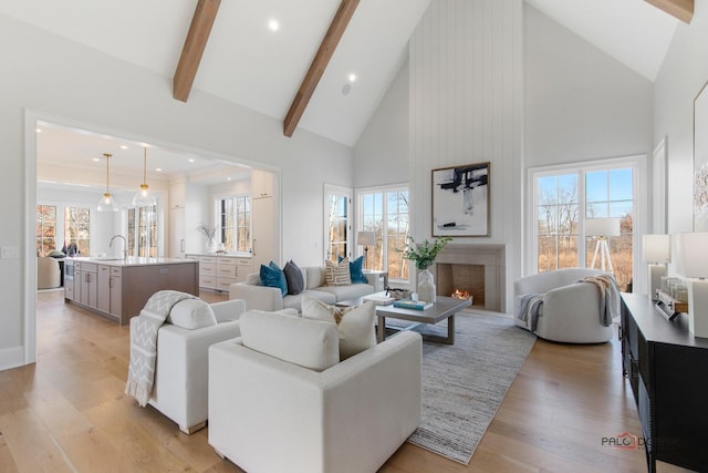 living room with high vaulted ceiling, beamed ceiling, a large fireplace, sink, and light wood-type flooring