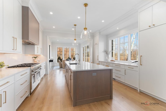 kitchen featuring decorative light fixtures, white cabinetry, sink, range with two ovens, and a kitchen island with sink