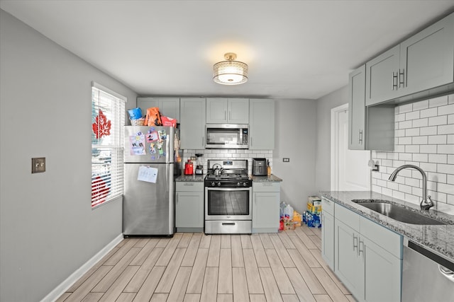 kitchen with appliances with stainless steel finishes, light hardwood / wood-style flooring, light stone counters, and sink