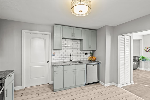 kitchen featuring appliances with stainless steel finishes, backsplash, dark stone counters, sink, and light hardwood / wood-style flooring