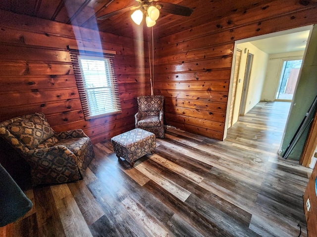 sitting room with hardwood / wood-style flooring, ceiling fan, and wood walls