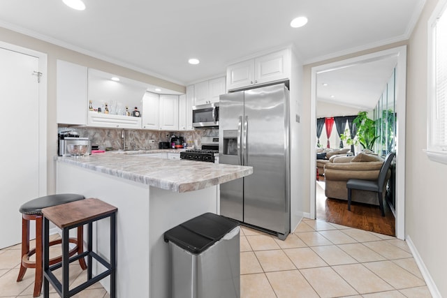 kitchen featuring white cabinets, ornamental molding, light hardwood / wood-style floors, a kitchen bar, and stainless steel appliances