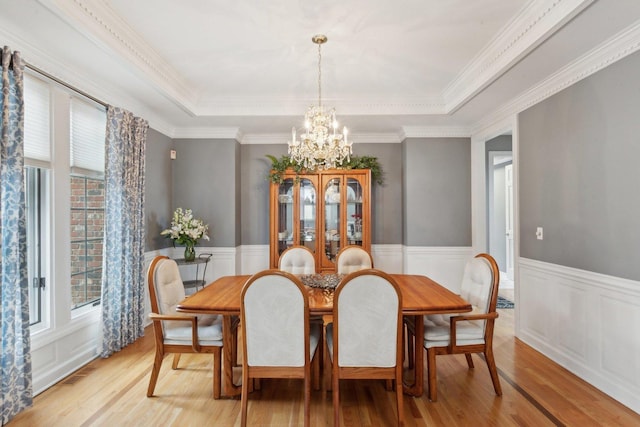 dining space featuring an inviting chandelier, a tray ceiling, light hardwood / wood-style flooring, and ornamental molding