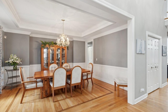 dining area featuring an inviting chandelier, a tray ceiling, light hardwood / wood-style flooring, and ornamental molding