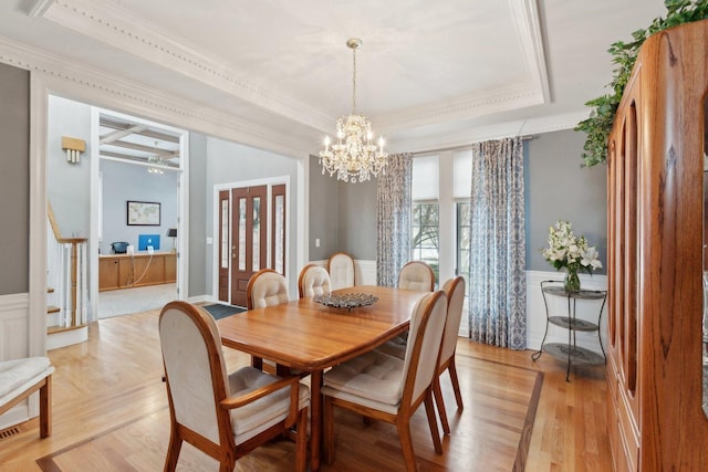 dining space with crown molding, a tray ceiling, an inviting chandelier, and light hardwood / wood-style flooring