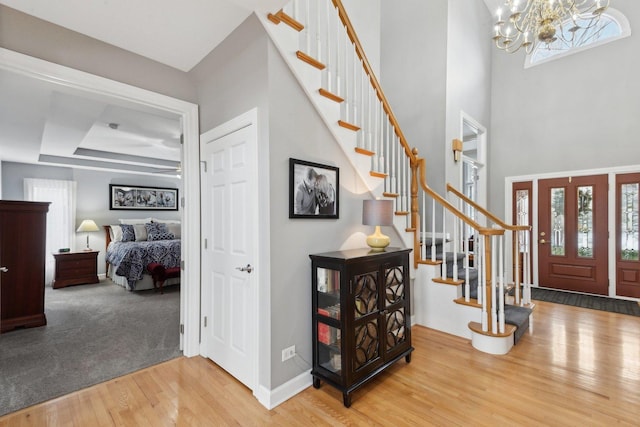 entryway with wood-type flooring, a towering ceiling, a notable chandelier, and a tray ceiling