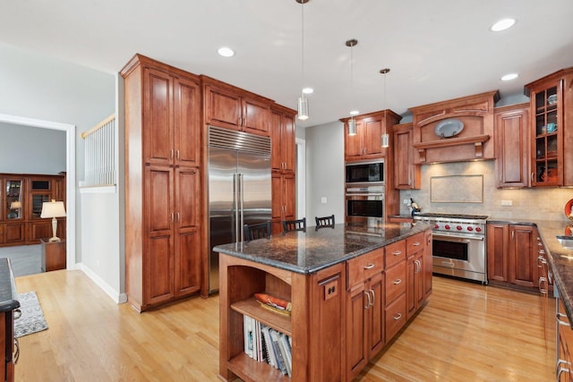 kitchen with a kitchen island, dark stone counters, hanging light fixtures, built in appliances, and light hardwood / wood-style floors